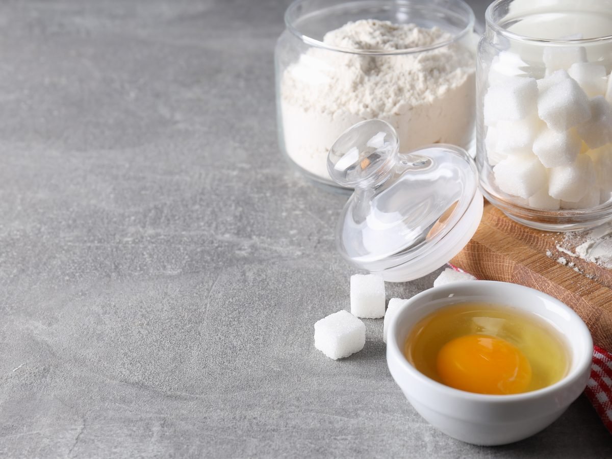 Baking station with flour, sugar cubes and a cracked egg in a bowl