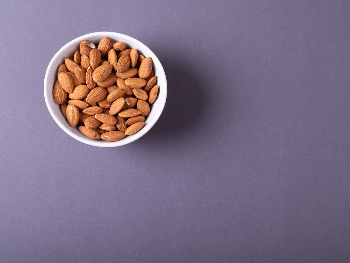 A white bowl of almonds on a plain background