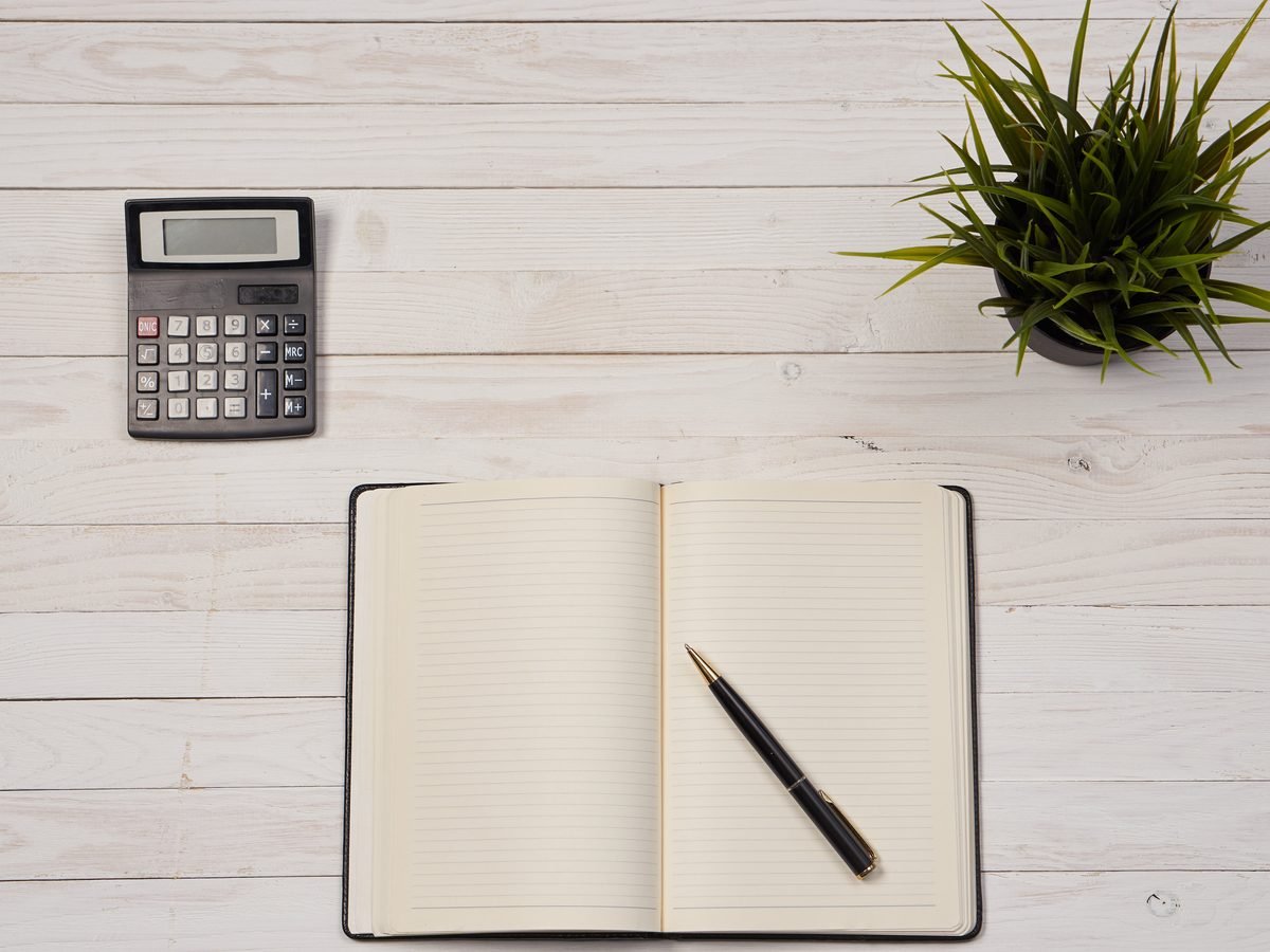 A calculator, open notebook and pen on a wooden desk